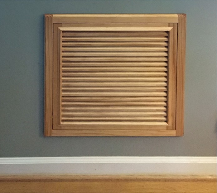 Stained wood return air vent cover in gray wall with white baseboard and wood floors